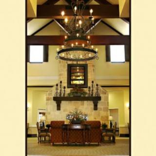 A spacious living room with a high ceiling, featuring a large chandelier and a stone fireplace.