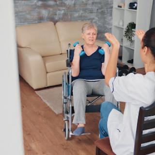 A caregiver assists an elderly patient in a wheelchair during a physical therapy session.