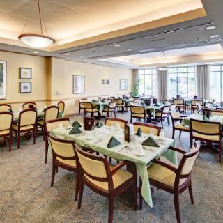 A well-lit dining room set up with neatly arranged tables and chairs, featuring green decorative elements.