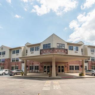 A view of a multi-story building with a covered entrance and parking area on a clear day.