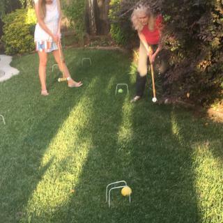 Two people playing croquet on a sunny lawn.