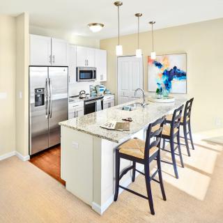 A modern kitchen with stainless steel appliances and a central island featuring bar stools and pendant lighting.