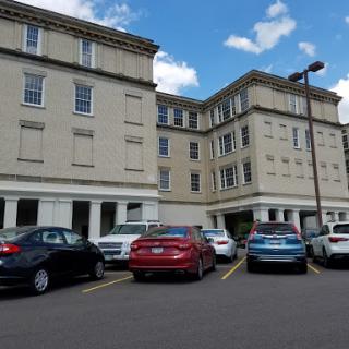 A view of a multi-story hotel building with parked cars in front under a partly cloudy sky.