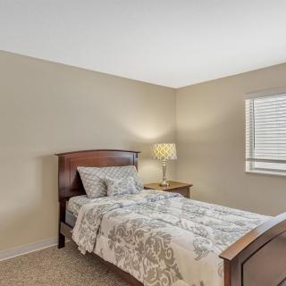 A cozy bedroom with a single bed, lamp, and window with blinds.