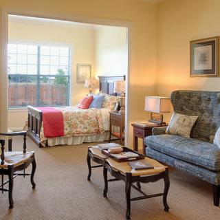 A cozy living area with a sofa and tables connected to a bedroom featuring a bed and large window.
