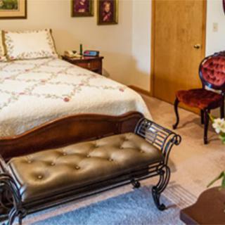 A cozy bedroom featuring a neatly made bed, an upholstered bench at the foot, and a vintage chair in the corner.