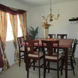 A dining room with a large wooden table and chairs, decorated with a chandelier and curtains.