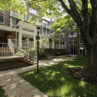 A serene view of a residential apartment complex with a well-maintained garden and shaded pathway.