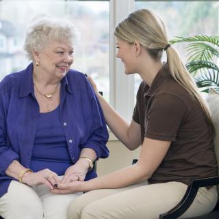 A caregiver and an elderly woman share a warm conversation indoors.