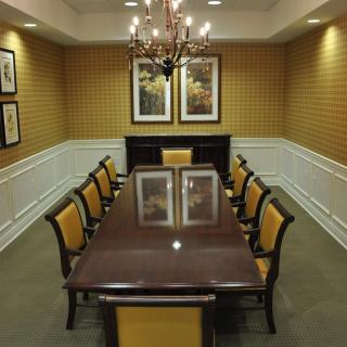 A formal conference room with a long table, surrounded by chairs and illuminated by a chandelier.