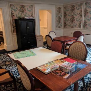 A cozy meeting room with floral wallpaper, a wooden table surrounded by chairs, and various items on the table.