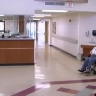 A hospital waiting area with a reception desk and a person in a wheelchair.