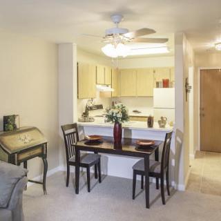 A cozy apartment interior featuring a small dining area with a table and chairs, adjacent to an open kitchen.