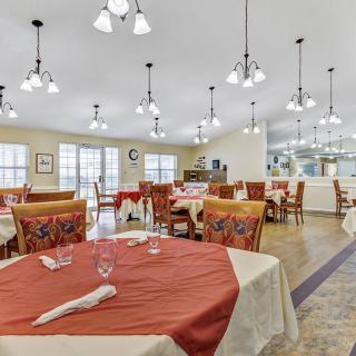 A spacious dining area with neatly arranged tables and chairs, adorned with red and white tablecloths, under warm interior lighting.