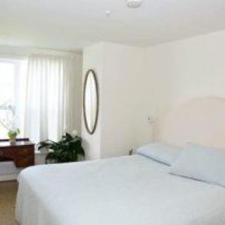 A well-lit bedroom with a large bed, mirror, and desk by the window.