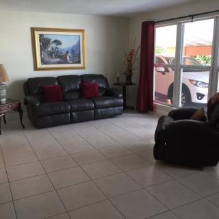 A living room with a sofa, armchair, painting on the wall, and a view of a car outside the window.