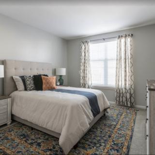 A cozy bedroom with a tufted headboard, patterned rug, and natural light streaming through the window.