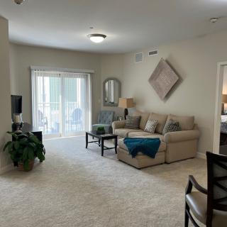 A cozy living room featuring a beige sofa, indoor plant, wall decor, and a sliding glass door leading to a balcony.