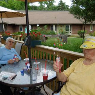 Two elderly individuals sitting on a patio enjoying ice cream on a summer day.