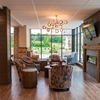 A modern lounge area with cozy seating, a stylish chandelier, and a fireplace, featuring large windows that allow abundant natural light.