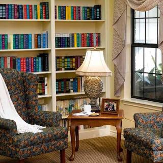 A cozy living room with bookshelves, two armchairs, and a lamp by the window.