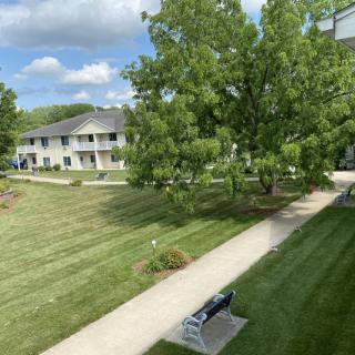 A serene view of an apartment complex with well-maintained lawns, trees, and a path leading through the area.