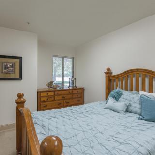 A cozy bedroom with a wooden bed frame, soft blue bedding, and a matching dresser near the window.