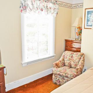A cozy bedroom with a floral armchair and natural light streaming through the window.