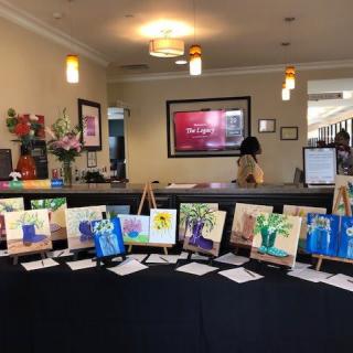 A collection of colorful paintings on easels displayed in a well-lit reception area.