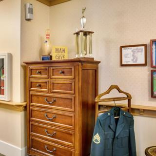 A room showcasing a wooden dresser with a trophy on top, a hanging jacket, and framed artwork on the wall.