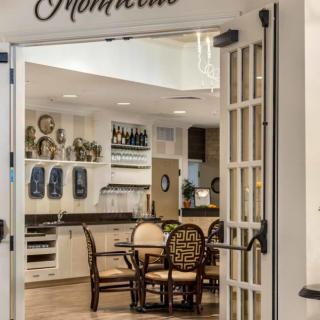A cozy kitchen and dining area viewed through open French doors, featuring a round table with chairs and decorative elements.