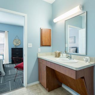 A modern bathroom with a vanity, sink, and large mirror, featuring a soft blue wall color.