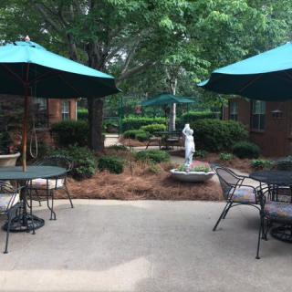 A serene outdoor patio area with tables, chairs, and umbrellas set among lush greenery and a small statue.