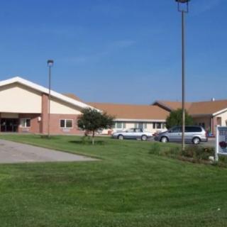 A nursing home with a spacious front lawn and parking area on a sunny day.