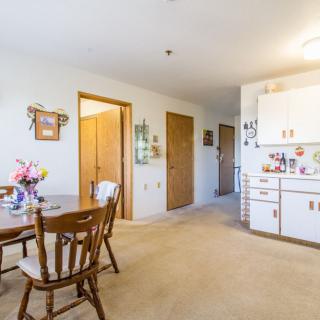 A cozy apartment interior featuring a dining area with wooden chairs and a table, adjacent to a compact kitchen.