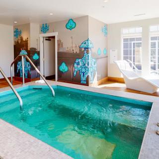 A modern indoor spa pool with mosaic tile accents and comfortable loungers, illuminated by natural light.