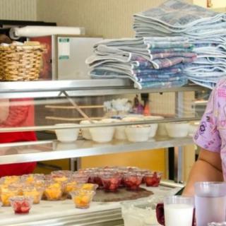 A cafeteria setting with a serving counter displaying cups of fruit and other food items.