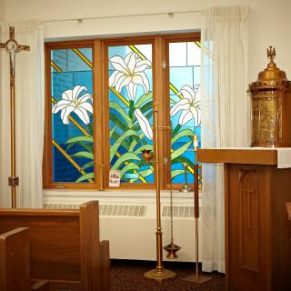 A serene chapel interior featuring a stained glass window with lilies.