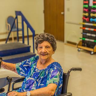An elderly woman in a wheelchair enjoys a moment of joy during her rehabilitation session.