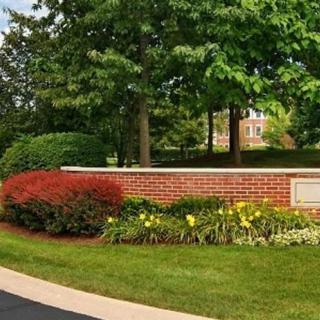 A scenic view featuring a brick wall surrounded by lush greenery, colorful flowers, and mature trees.