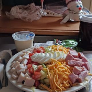A colorful salad platter featuring turkey, ham, cheese, and fresh vegetables.
