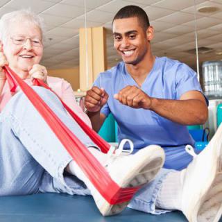 An elderly woman participating in a physical therapy session with a healthcare professional assisting her.