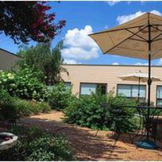 A tranquil garden patio with outdoor seating and umbrellas under a blue sky.
