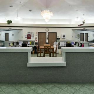 An empty office space with a central table and chairs, surrounded by workstations.