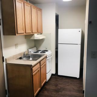 A compact apartment kitchen with wooden cabinets, a refrigerator, stove, and sink.