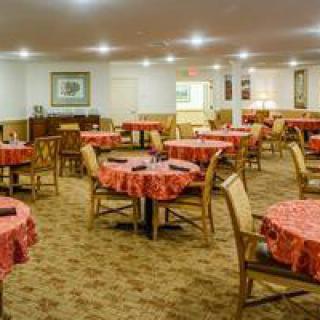 An empty dining room with neatly arranged tables and chairs, featuring a carpeted floor and warm lighting.
