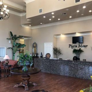 A spacious and elegant lobby with a reception desk, decorative plants, and a chandelier.