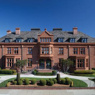 A large brick mansion with intricate landscaping and a clear blue sky.