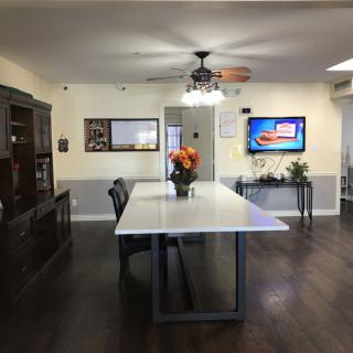 A modern dining room with a large table, flowers centerpiece, and a television on the wall.