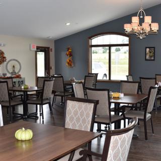 A cozy dining room with several tables and chairs, decorated with small pumpkins and a chandelier.